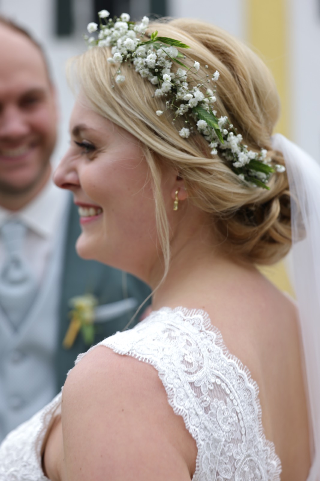 Braut mit Blumenkranz im Haar, Bräutigam im Hintergrund